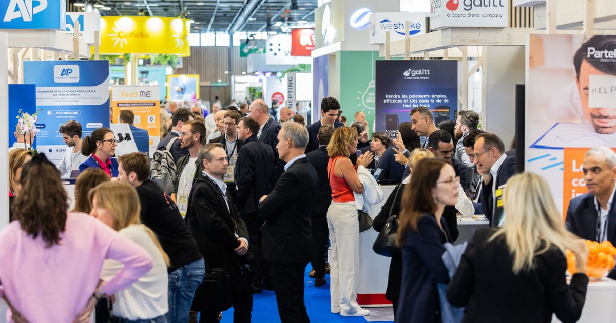 Lively scene in the aisles of a trade show with numerous visitors and exhibitors interacting around booths, showcasing a dynamic and friendly atmosphere.