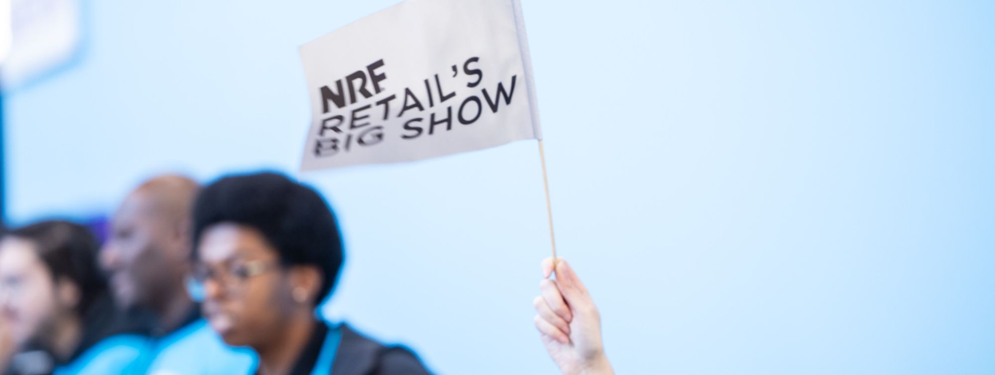 Raised hand holding a flag marked "NRF Retail’s Big Show".